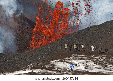 KAMCHATKA PENINSULA, RUSSIA - FEB 2, 2013: Eruption Tolbachik Volcano on Kamchatka, tourists climbing on background fountain of lava erupting from crater of volcano. Russian Far East, Kamchatka Region