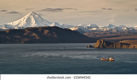 Kamchatka Peninsula, Small craft sails out of Avacha Bay. In the background Vilyuchinsky volcano already covered with snow.