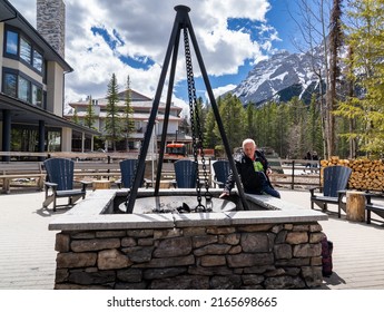 Kananaskis Alberta Canada, June 05 2022: A Tourist Reaching Out To An Outdoor Fire Pit At The Marriott Mountain Lodge.