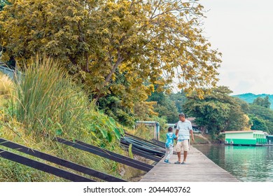 KANCHANABURI, THAILAND-SEPTEMBER 5,2020 : Unidentified Asian Grandfather And Grandchild Wear Protective Face Mask To Prevent Coronavirus (COVID-19) Walking On Wooden Bridge Along River At Din Cafe.