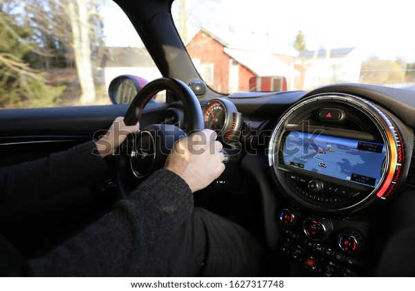 Kangasala, Finland - January 25 2020: Man driving\
a small car (Mini John Cooper Works) uses integrated GPS satellite\
navigation system to reach his destination. Closeup of hands and a\
steering wheel.