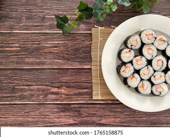Kani Maki (Crab stick Sushi rolls) Japanese food in a white plate on a wooden background. Selective focus. Flat lay. Grainy wooden surface.