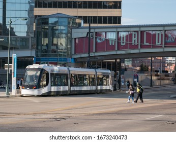 Kansas City, MO / United States Of America - February 18th, 2020 : Two Pedestrians Cross Main St In KC With Electric Street Car And Skyway In Background.  Winter City In Daylight, People Commuting.