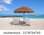 Kapalina Beach Ewa Beach HI. White sand beach with thatched roof umbrella and white Adirondack chairs.  Blue pacific ocean with view of Diamond Head and Waikiki across the ocean.