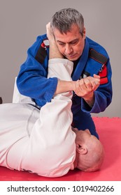 Kapap and brazilian jiu jitsu instructor in traditional kimono demonstrates ground fighting arm lock techniques with his student