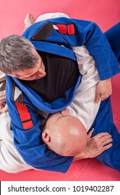 Kapap and brazilian jiu-jitsu instructor in traditional kimono demonstrates ground fighting techniques with his student