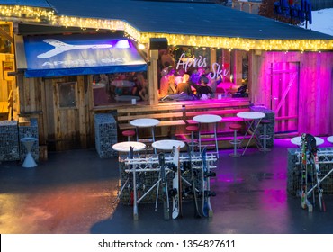 KAPRUN, AUSTRIA, March 13, 2019: Nigt Outdoor View On Illuminated Apres Ski Restaurant Next To Kaprun Cable Station Where People Are Drinking And Having Fun After Skiing