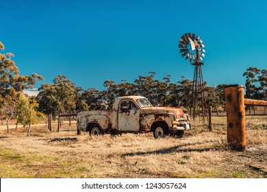 Kapunda, South Australia - June 17, 2017: Rusty Holden FJ Ute and vintage Kookaroo windmill on display near farm entrance from highway