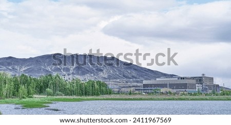 Karabashmed copper smelter, Karabash, Russia. Behind building are bald lifeless mountains. Industrial landscape. Place is currently being revived. City cleared pond in foreground