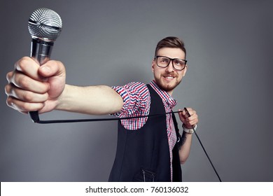 Karaoke man sings the song to microphone, singer with beard on grey background. Funny man in glasses holding a microphone in his hand at the karaoke singer sings the song