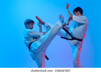 Karate fight. Studio shot of sports training of two karatedo fighters in doboks isolated on blue background in neon. Concept of combat sport, challenges, skills. Sportsmen practicing base technique