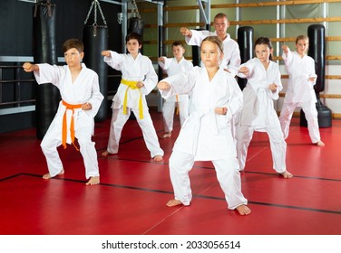 Karate Kids In Kimono Performing Kata Moves With Their Teacher In Gym During Group Training.