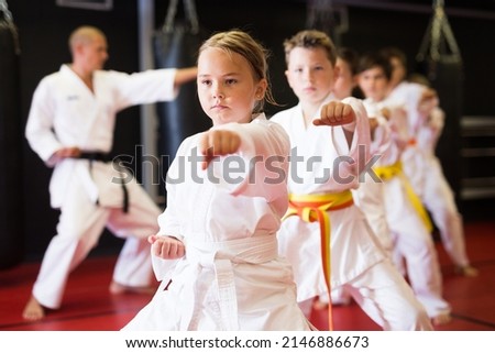 Karate kids in kimono performing kata moves with their teacher in gym during group training.
