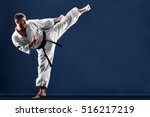 Karate man in a kimono hits foot on a blue background