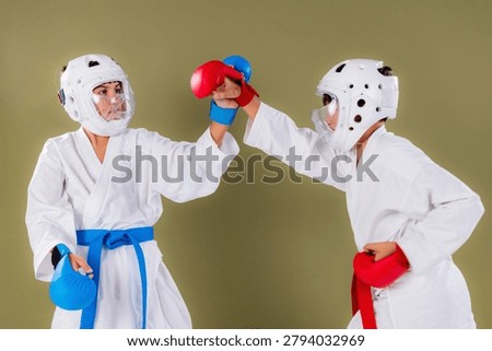  Karate practitioner raises a red gloved punch toward the opponent's head while the defender intercepts with an upward block, demonstrating high guard defensive technique during a competitive sparring session.