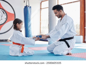 Karate, promotion and student with blue belt for learning, training and kid practice taekwondo. Martial arts, teacher and people in class for reward, success and master giving girl child obi in gym - Powered by Shutterstock