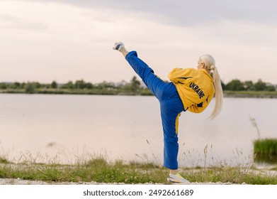 Karate woman in sportswear demonstrates a high kick outdoors in the park - Powered by Shutterstock