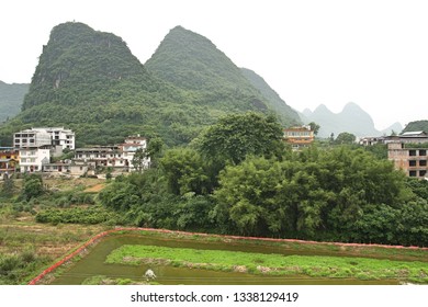 Karst mountain peaks in Yangshuo, China with houses, low-rise buildings, trees and irrigated field in foreground and silhouetted peaks in background - Shutterstock ID 1338129419