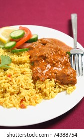 A Kashmiri Lamb Curry With Rice And A Fork On A Plate Ove A Maroon Tablecloth.