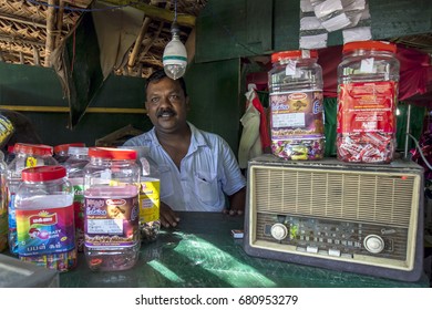 KATARAGAMA, SRI LANKA - NOVEMBER 16, 2015 : A Sri Lankan Shop Keeper Near Kataragama In Sri Lanka. In The Foreground Is His Old Transistor Radio And Numerous Lolly Jars.