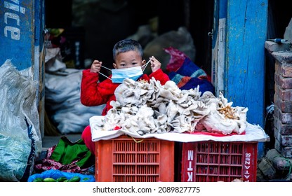 KATHMANDU, NEPAL - December 11, 2021: Child Wearing Mask And Selling Vegetables On Street Market, Daily Stuggle Life Of Street Vendor During Covid Pandemic At Kathmandu.
