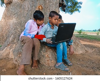 Katni, INDIA - January 1, 2020: Indian Poor Kid Boys Operating Laptop Computer Down The Tree Shadow At Open Area Environment 