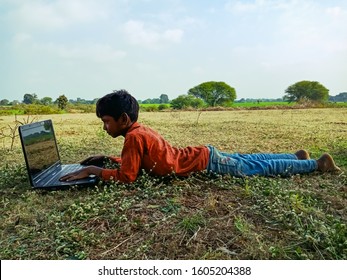 Katni, INDIA - January 1, 2020: Asian Poor Kid Lying On Grass Operating Laptop Computer System At Natural Background 