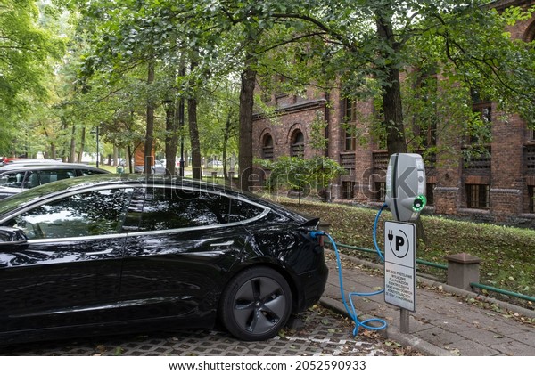 Katowice, Poland -\
September 24, 2021. A static shot of a solid black Tesla Model 3\
dual motor charging at the EVBox AC charging station in a cloudy\
autumn day. Selective\
focus.