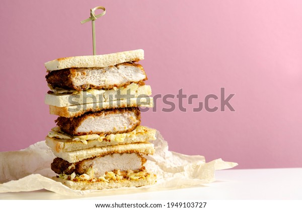 Katsu sandos\
japanese sandwich with chicken or pork chop, cabbage and tonkatsu\
sauce isolated on pink\
background.