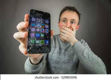 KAUNAS, LITHUANIA - DECEMBER 5, 2016: Desperate and astonished man holds cracked smartphone . Screen broken smartphone. Cracked iphone 4. Broken phone