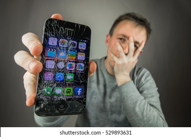KAUNAS, LITHUANIA - DECEMBER 5, 2016: Desperate and astonished man holds cracked smartphone . Screen broken smartphone. Cracked iphone 4. Broken phone