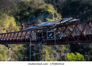 Kawarau Bridge, New Zealand, October 6, 2019: Modern European Boy Preparing To Bungee Jump With The New Zealand Flag At His Side