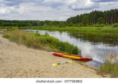 A Kayak Boat With Paddleboards  Moored To The Riverbank