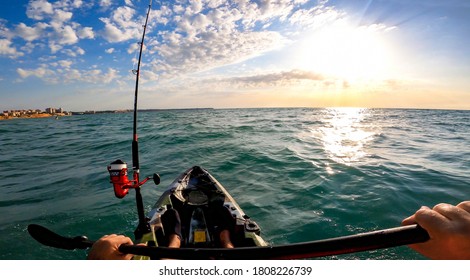 Kayak fishing, trolling fishing. Fisherman trolling in kayak at mediterranean sea on a windy day with waves during sunset. Aquatic summer sports. Kayaker trolling and fishing at sea in his canoe.