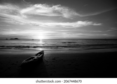 A kayak lies on the tropical beach during a sunset. Black and white photo.