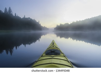 Kayak surfer on a  misty lake by early morning in Quebec, Canada