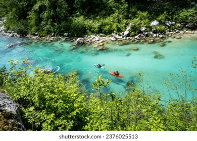 Kayakers riding beautiful Soca river rapids in turquoise colour, carving the deep canyon in the mountains of Slovenian Alps