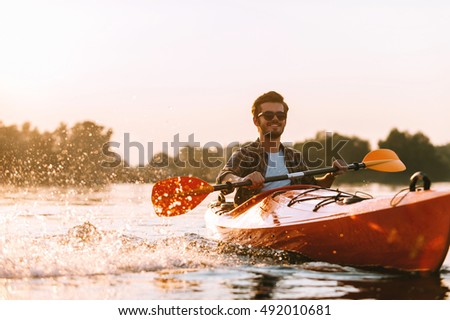 Kayaking on river. Handsome young smiling man splashing water while kayaking on river