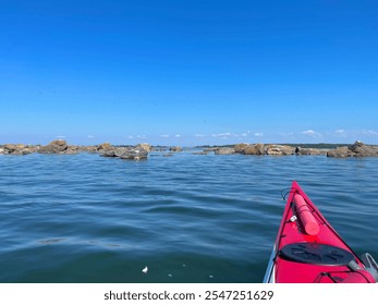 Kayaking through the Finnish archipelago on a sunny summer day. A vibrant red kayak moves through calm blue water and rocky formations. Peaceful outdoor adventure ideal for travel and recreation. - Powered by Shutterstock