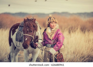 Kazakh Girl Eagle Hunters In Traditionally Wearing Typical Mongolian Dress Culture Of Mongolia She Rider Horse On Altai Mountain Background At Ba-yan UlGII, MONGOLIA