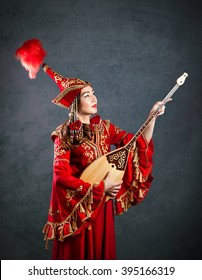 Kazakh Woman In Red Costume Playing Dombra Kazakh Musical Instrument At The Grey Background