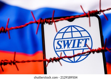 Kazan, Russia - Feb 25, 2022: SWIFT financial system logo on smartphone screen behind barbed wire on background of Russian flag. Sanctions against Russia, disconnection from SWIFT.