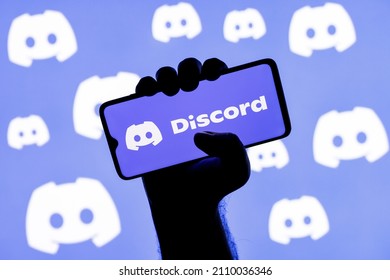 Kazan, Russia - Jan 20, 2022: Smartphone With The Discord Social Gaming Platform Logo On The Screen In A Clenched Hand On The Background Of Discord Logos