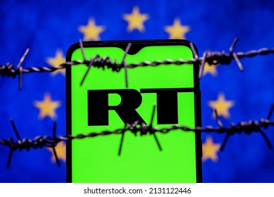 Kazan, Russia - Mar 02, 2022: Smartphone with RT (Russia Today) logo on background of flag of European Union behind barbed wire. Russia Today network banning in EU.