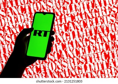 Kazan, Russia - Mar 02, 2022: Smartphone with Russia Today logo in hand on background of inscriptions sanctions, censored, banning, blocking and others. RT ban on broadcasting in different countries.