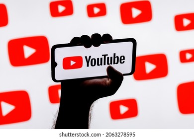 Kazan, Russia - Oct 24, 2021: Smartphone with the Youtube social media platform logo on the screen in a clenched hand on the background of Youtube logos