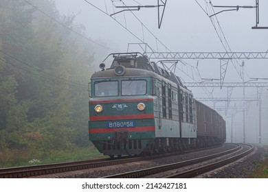 Kazatin, Ukraine - autumn 2021: powerful green locomotive VL80 pulls long train of freight cars loaded with grain and corn to the seaport Odessa. Freight railway transportation. Transnational route. 