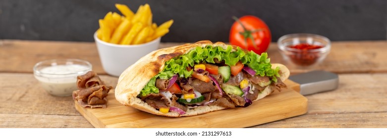 Döner Kebab Doner Kebap slice fast food in flatbread with French Fries on a wooden board panorama sliced