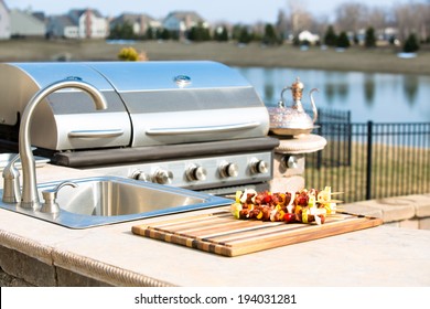 Kebabs lying on a wooden board on the counter of an outdoor summer kitchen alongside the gas BBQ ready to be cooked for a healthy lunchtime snack