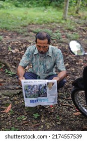 Kebumen, Indonesia - February, 2016: An Old Man Reading A Newspaper While Squatting Down.